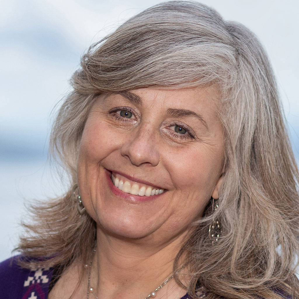 A woman with long grey hair smiling for the camera.